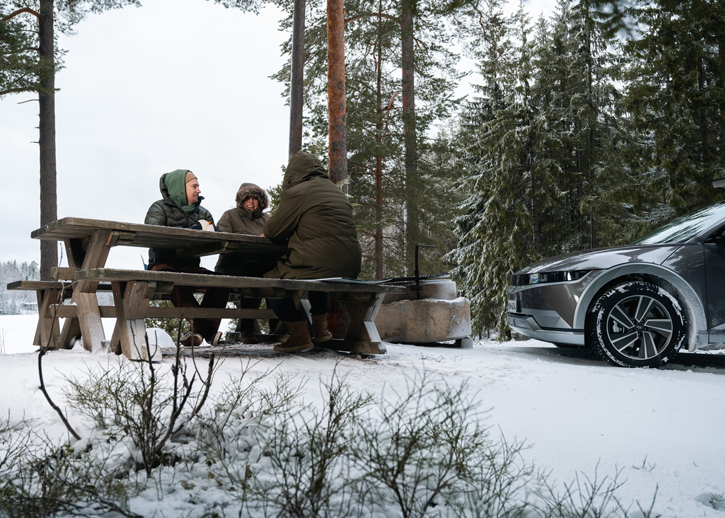 People sat round a picnic bench in snow next to a car