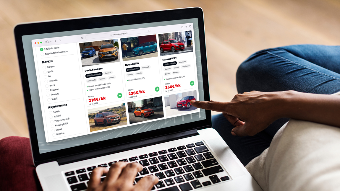 Laptop screen displaying Autoverkkokauppa website with hand pointing to screen