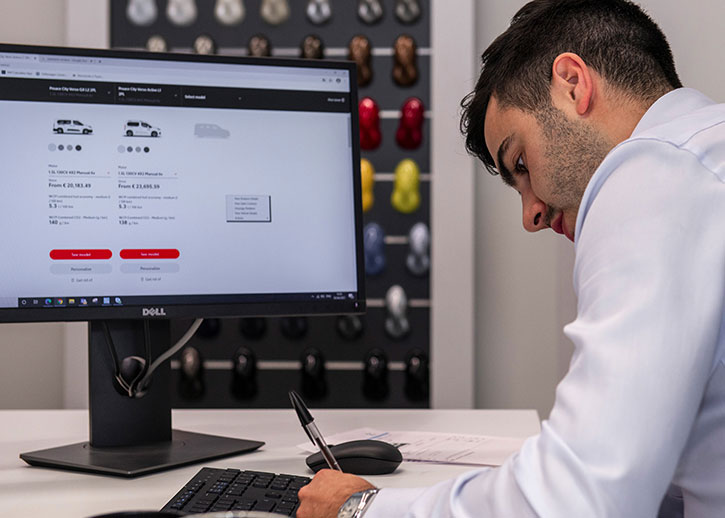 Person sat at desk writing with a computer in the background