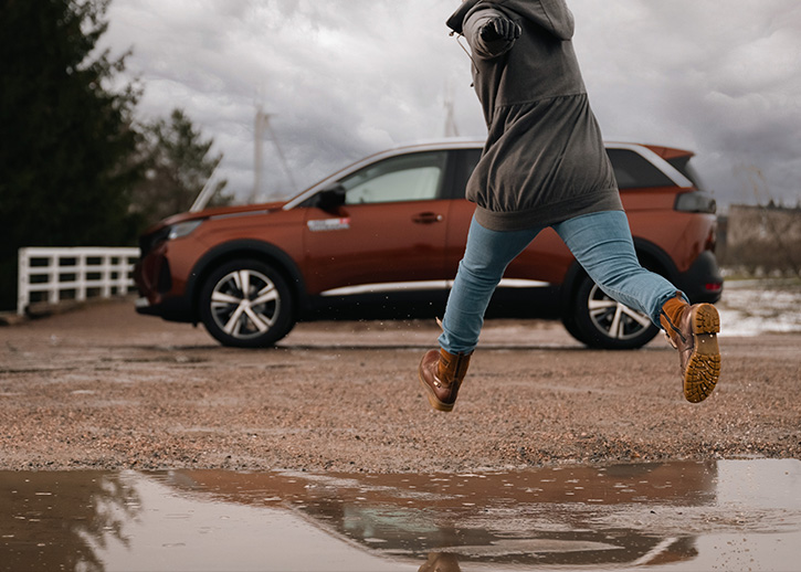 Person jumping over a puddle with a car in the background